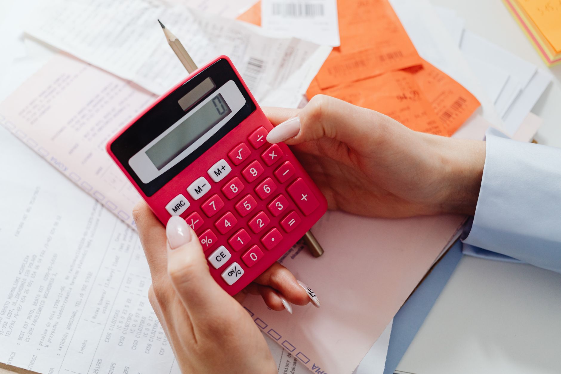 Mãos usando uma calculadora rosa sobre recibos e papéis de contas
